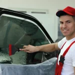 Smiling technician using a squeegee to apply tint film on a car window, representing professional and friendly Window Tinting Apopka services.