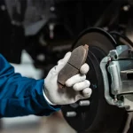 Technician holding a worn brake pad near a vehicle’s braking system, highlighting professional diagnostics and replacement during Brake Repair Apopka services at Ruben’s Tires.