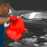 Technician in red gloves pouring oil into a vehicle engine, demonstrating professional and efficient Oil Change Apopka service at Ruben’s Tires.